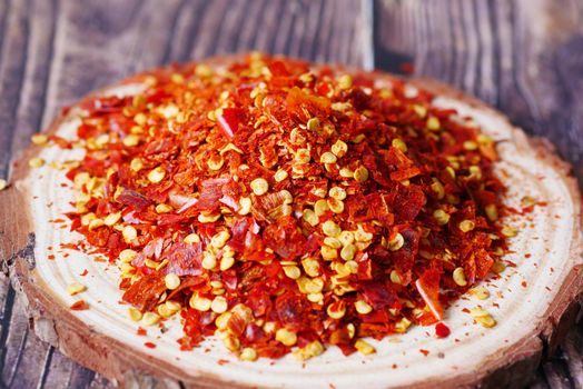 dried peppers flakes on a wooden plate on table ,