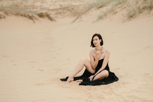 girl in a black long dress in a sandy desert under a blue sky