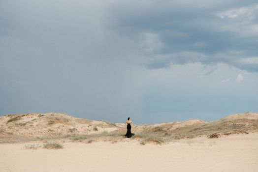 girl in a black long dress in a sandy desert under a blue sky