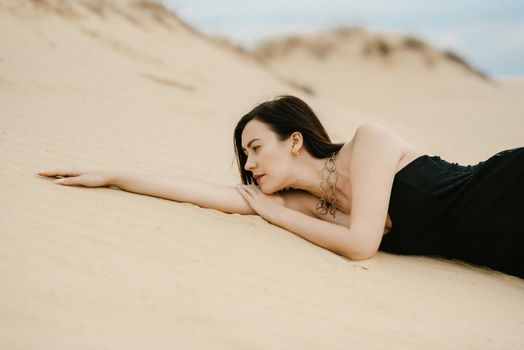 girl in a black long dress in a sandy desert under a blue sky