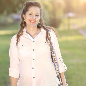 beautiful pregnant woman with a bag on his shoulder on the background of a Park on a Sunny day