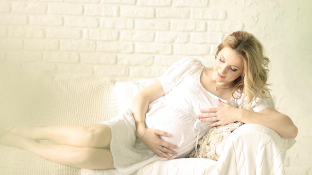 Happy pregnant woman sitting on sofa at home in the bedroom