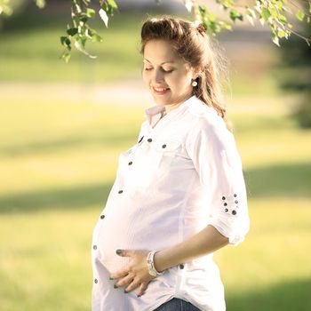 Beautiful pregnant woman relaxing outside in the Park looking at the belly