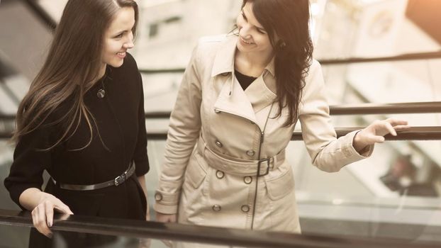 Two business people on the escalator, two young entrepreneurs talk about work plans, smiling and looking at each other