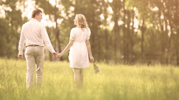 Happy couple - pregnant woman and her husband go on a picnic on the grass. They look at each other