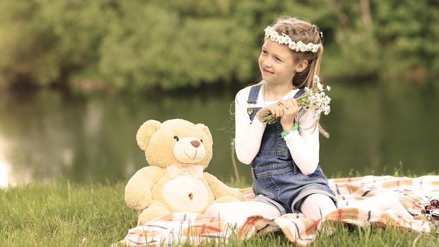 little girl with a soft toy on a picnic near the river on a Sunny day