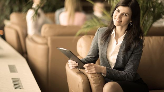 Successful business woman with documents sitting in a chair against a background of a modern office