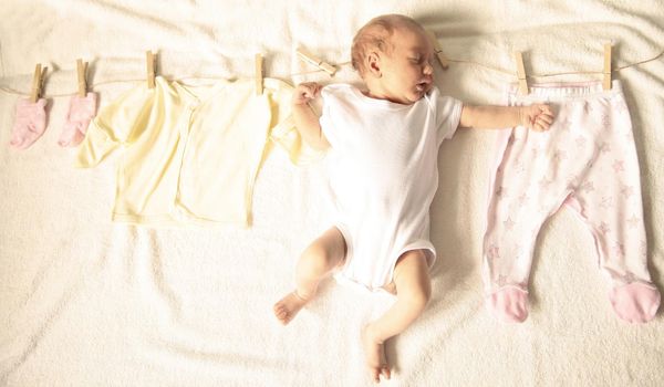 sleeping newborn baby and children's clothes on a wooden primako on a light background