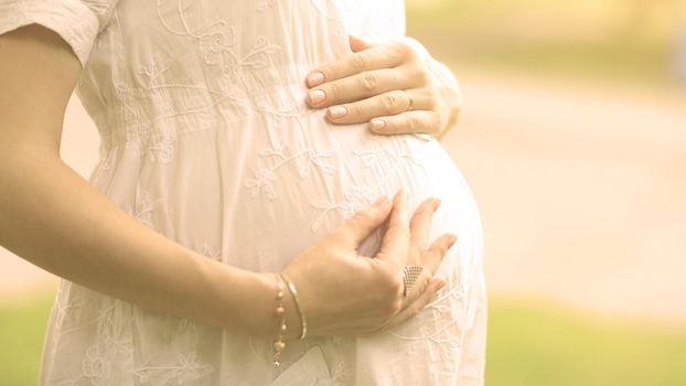 Image of pregnant woman touching her belly with hands on a bright sunny day