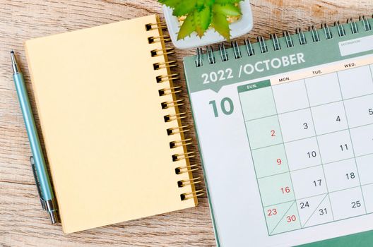 The October 2022 desk calendar and diary with small plant on wooden background.