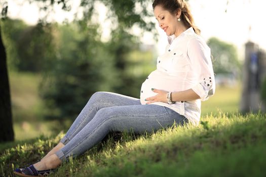 pregnant woman sitting on the grass in a Park on a Sunny day