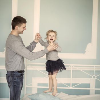 loving father plays with happy little daughter on the bed in the bedroom