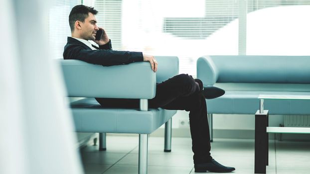 businessman sits in the lobby of a modern office and talking on the phone.the photo has a empty space for your text