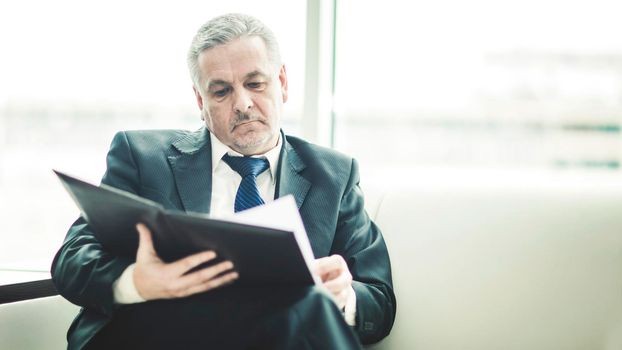 experienced businessman studies working papers sitting on a white sofa in a private office