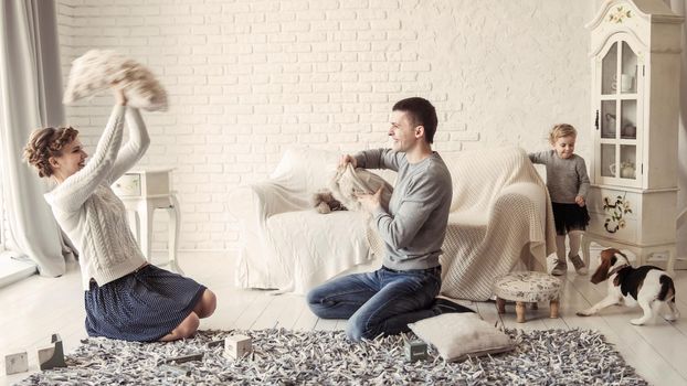 mother,father,five year old daughter and pet dog playing with pillows in the spacious living room on Sunday