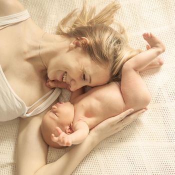 happy motherhood concept - happy mother and newborn baby on a white blanket