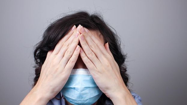 Woman wearing protection face mask against coronavirus covering her eyes with hands. Woman in a mask hiding her eyes. Medical mask, Close up shot, Select focus, Prevention from covid19