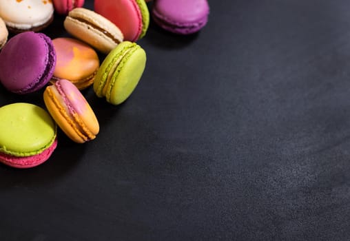 Assorted colorful french cookies macaroons on a black background. Space for text. Closeup. Top view. Concept of the baking macaroons