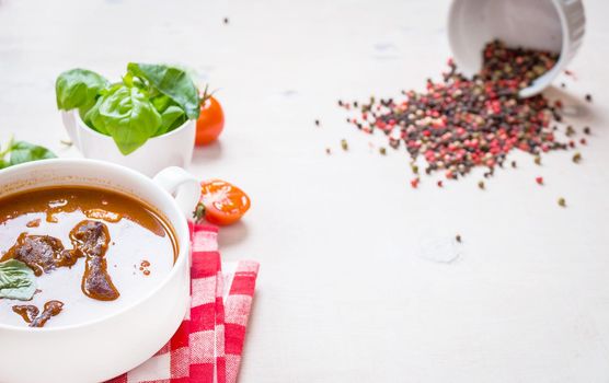 Tomato soup with meat on a white rustic wooden table with fresh cherry tomatoes, basil, dry pepper and red gingham kitchen towel. Ingredients for soup. Soup background. Space for text