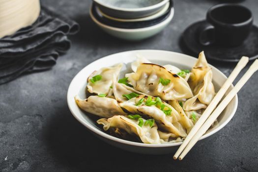 Asian dumplings in bowl, chopsticks, bamboo steamer, plates. Asian table setting. Chinese dumplings for dinner. Selective focus. Asian style decoration. Chinese fresh homemade food. Closeup