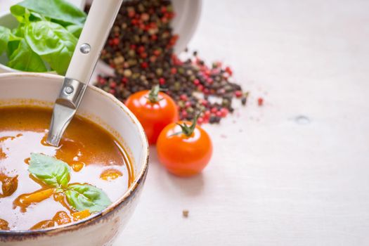 Tomato soup with meat on a white rustic wooden table with fresh cherry tomatoes, basil, dry pepper and red gingham kitchen towel. Ingredients for soup. Soup background. Space for text