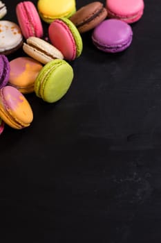 Assorted colorful french cookies macaroons on a black background. Space for text. Closeup. Top view. Concept of the baking macaroons