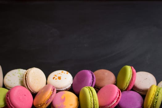 Assorted colorful french cookies macarons on a black background. Space for text. Closeup. Top view. Concept of the baking macarons