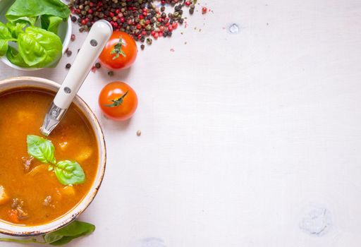 Tomato soup with meat on a white rustic wooden table with fresh cherry tomatoes, basil, dry pepper and red gingham kitchen towel. Ingredients for soup. Soup background. Space for text