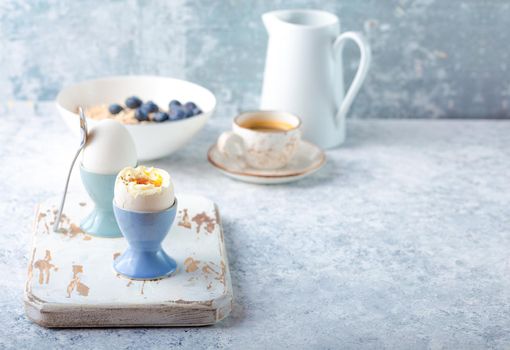 Fresh soft boiled eggs, oatmeal with berries, coffee, milk. White concrete rustic background. Soft eggs, healthy breakfast. Space for text. Selective focus. Tasty light fitness breakfast concept