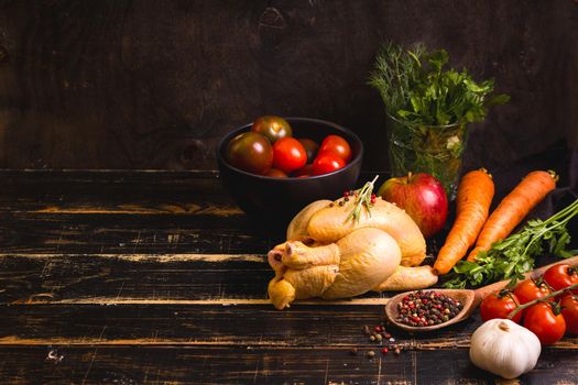 Raw whole chicken ready for cooking. Chicken, vegetables, herbs, spices on black rustic wooden background. Space for text. Food frame. Diet or healthy eating. Ingredients for cooking. Selective focus