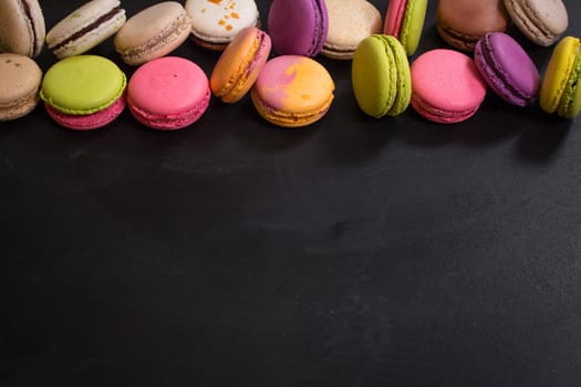 Assorted colorful french cookies macarons on a black background. Space for text. Closeup. Top view. Concept of the baking macarons