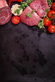 Raw juicy meat ready for roasting on a black chalk board background. Veal fillet with cherry tomatoes, hot pepper and herbs. Space for text