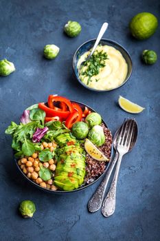 Bowl with healthy salad and dip. Close-up. Buddha bowl with chickpea, avocado, quinoa seeds, red bell pepper, fresh spinach, brussels sprout, lime mix. Vegetarian salad. Clean healthy eating concept