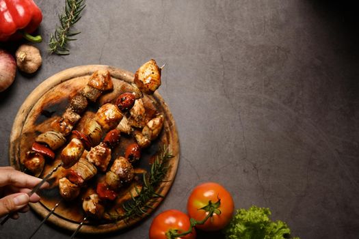 Above view hand holding tasty grilled chicken skewers with tomato, sweet pepper and onions. Copy space for your text.