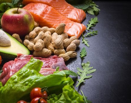 Fresh vegetables, fruits, fish, meat, nuts on black chalk board background. Сauliflower, avocado, apples, tomatoes, salmon, beef, spinach, herbs. Diet/healthy/paleo food. Ingredients. Space for text