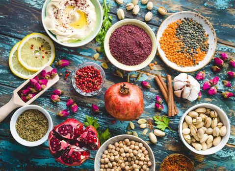 Arab ingredients for middle eastern food. Arabic cuisine ingredients on blue wooden background. Hummus, chickpea, lentils, rose buds, spices, pomegranate, pistachios. Halal food making. Top view