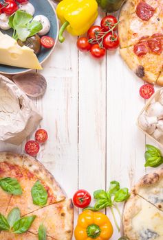 Pizza with assorted toppings and ingredients background. Space for text. Pizza, flour, cheese, tomatoes, basil, pepperoni, mushrooms and rolling pin over white wooden background. Top view. Food frame