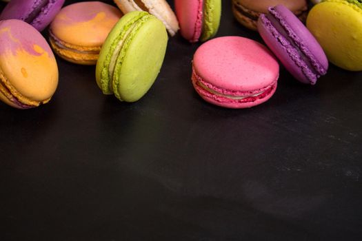 Assorted colorful french cookies macaroons on a black background. Space for text. Closeup. Top view. Concept of the baking macaroons