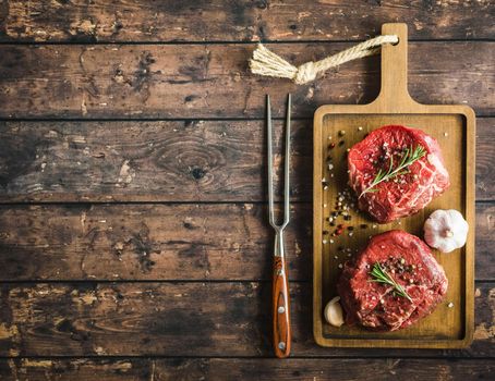 Raw marbled meat steak Filet Mignon with seasonings, fork, wooden cutting board. Space for text. Beef steak ready for cooking. Top view. Ingredients. Uncooked meat steak. Close-up. Rustic background