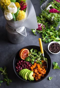 Festive table with fresh clean organic food. Quinoa vegetables salad in bowl, salad leaves, flowers bouquet. Superfood or detox eating concept. Spring table setting. Vegan/vegetarian food. Make salad