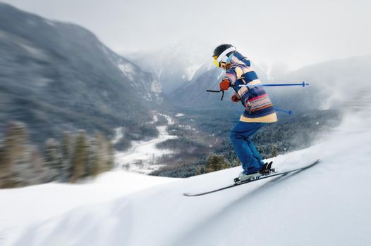 A female athlete skier rides a freeride in a winter forest in the mountains. Jump against the backdrop of snow-covered trees and the setting sun.