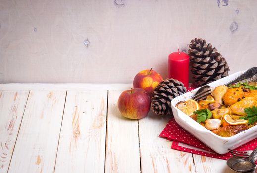 Roasted chicken. Christmas food background. Celebration white wooden table with roasted chicken, apples, decorated with candles, cones, vintage cutlery. Christmas/Thanksgiving dinner. Space for text