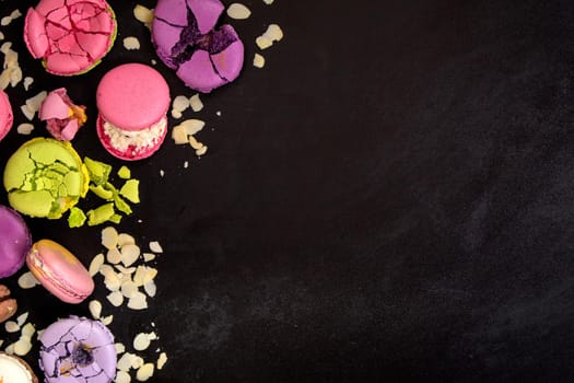Assorted colorful french macarons and almond flakes on a black background. Space for text. Closeup. Top view. Concept of the baking macarons