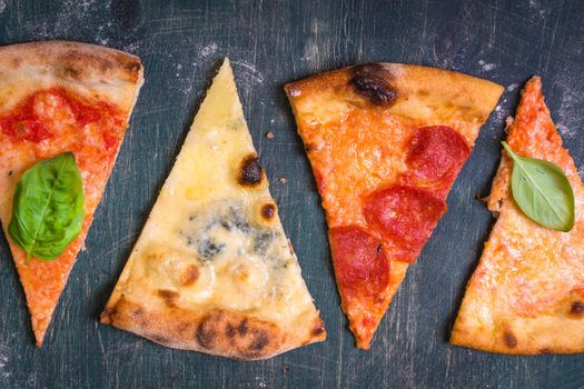 Assorted pizza slices. Margherita, pepperoni, four cheese pizza. Top view. Different types of pizza on the textured old wooden table.