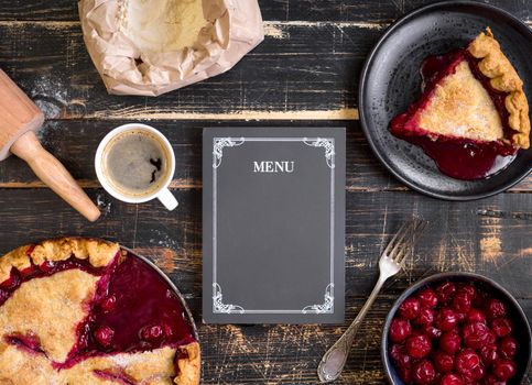 Baking background with sliced cherry pie, flour, rolling pin and menu chalkboard on the black wooden table. Ingredients for baking/dessert or pie making