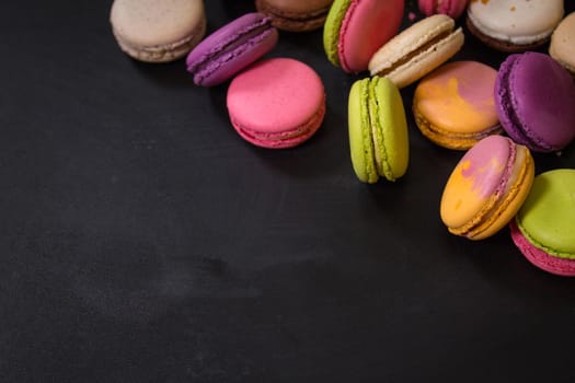 Assorted colorful french cookies macaroons on a black background. Space for text. Closeup. Top view. Concept of the baking macaroons