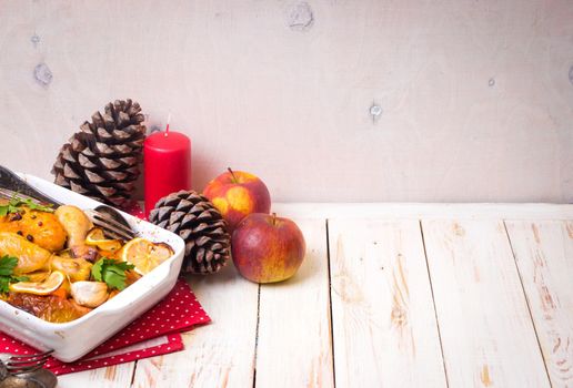 Roasted chicken. Christmas food background. Celebration white wooden table with roasted chicken, apples, decorated with candles, cones, vintage cutlery. Christmas/Thanksgiving dinner. Space for text