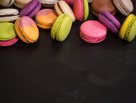 Assorted colorful french cookies macaroons on a black background. Space for text. Closeup. Top view. Concept of the baking macaroons