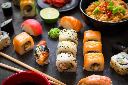 Table served with sushi and traditional japanese food on dark background. Sushi rolls, hiyashi wakame, miso soup, ramen, fried rice with vegetables, nigiri, soy sauce, сhopsticks. Japanese dishes set....