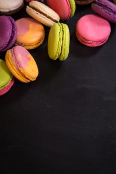 Assorted colorful french cookies macaroons on a black background. Space for text. Closeup. Top view. Concept of the baking macaroons